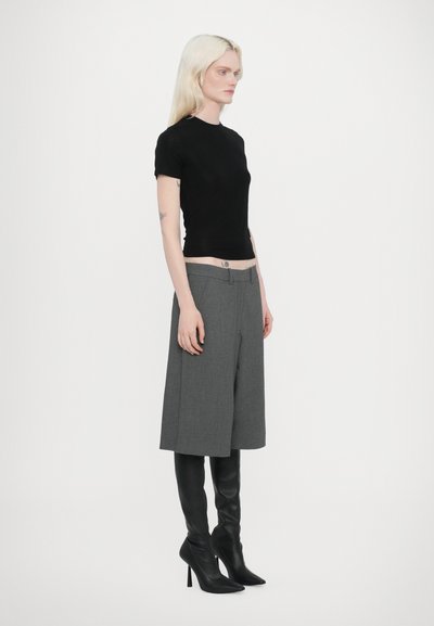 Haut noir à manches courtes, culottes grises ajustées et bottes noires à talons hauts arrivant au genou. Tissu lisse, silhouette ajustée et design structuré.