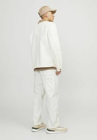 White denim jacket, brown collar over a tan shirt, paired with white cargo pants and beige sneakers. Features relaxed fit and sporty design.
