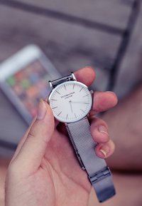 Reloj de malla plateada con esfera blanca, diseño minimalista y marcadores de hora delgados. Nombre de la marca "Victoria Hyde" visible en la carátula.