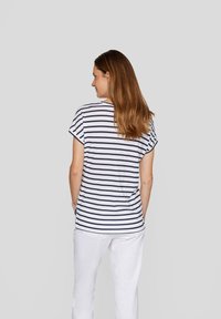 Striped T-shirt in navy and white, short sleeves, relaxed fit, with a scoop neckline and rounded hem, worn with white trousers.