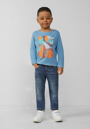 Lichtblauwe longsleeve shirt met kleurrijke grafische tekst, gecombineerd met donkerblauwe jeans en witte sneakers. Eenvoudig ontwerp en casual pasvorm.