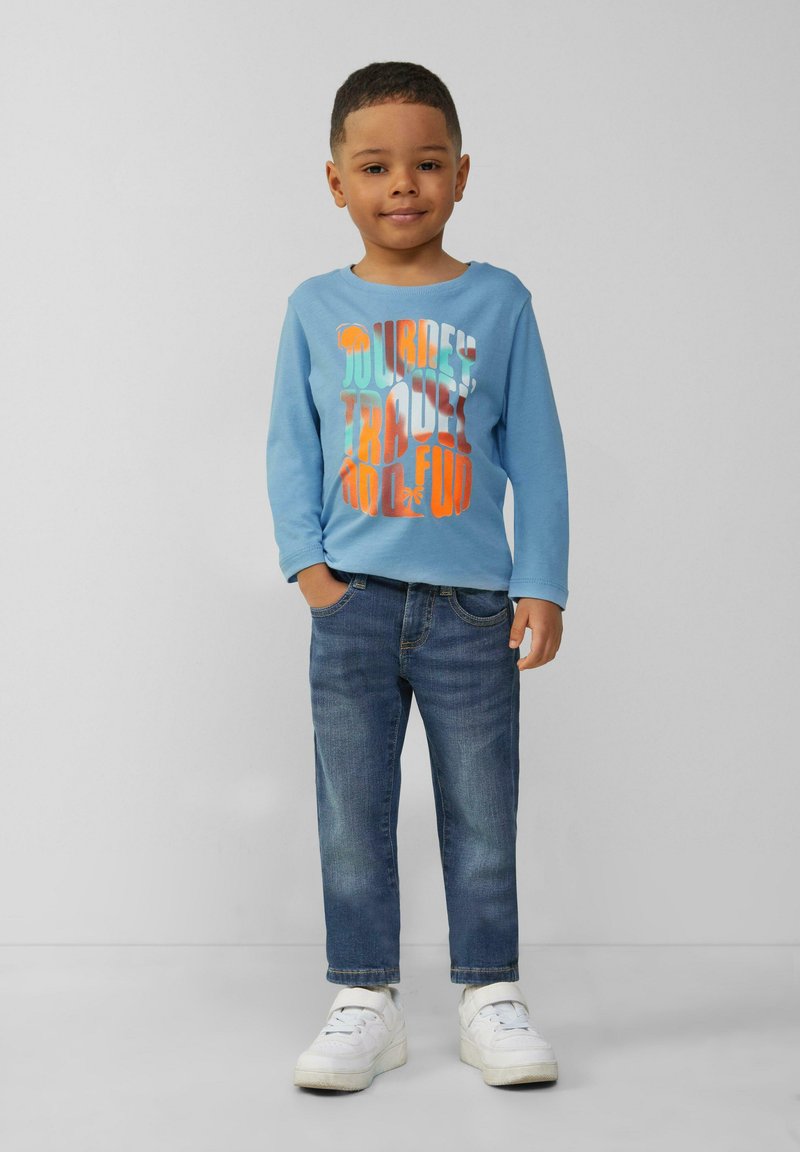 Lichtblauwe longsleeve shirt met kleurrijke grafische tekst, gecombineerd met donkerblauwe jeans en witte sneakers. Eenvoudig ontwerp en casual pasvorm.