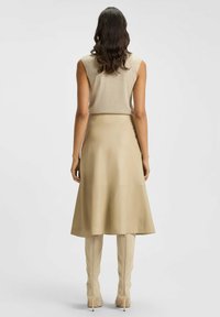 Beige Leder-Midirock mit glatter Textur, ausgestelltem Design und diagonalen Nähten. Kombiniert mit kniehohen beigen Stiefeln.