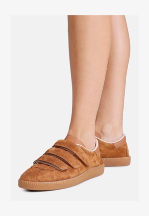 Brune ruskind sko med tre velcro-stropper, rund tå, gummisål og pink interiørdetaljer, vist fra en skrå sidevinkel.