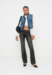 Denim vest med to frontlommer, paret med en hvit avkortet topp og svarte bukser med vide ben. Aksentuert med svarte høye hæler og en liten veske.