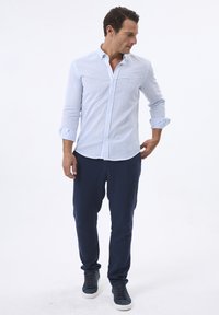 Camisa de manga larga a rayas azul claro y blanca con cuello abotonado, combinada con pantalones azul oscuro y zapatillas casuales. Textura de tela suave.