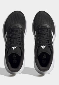 Un par de zapatillas de running Adidas en blanco y negro con parte superior de malla, cordones y el texto "Fin al Plástico" en el interior, sobre un fondo blanco.