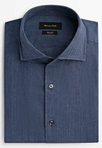 Chemise en lin bleu à manches longues, pliée, avec col classique et deux boutons visibles, avec une étiquette noire à l'intérieur du col.
