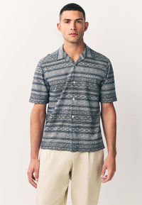 Kurzärmeliges Hemd in Marineblau mit einem geometrischen weißen Muster, ausgestattet mit einem Kent-Kragen und einer lockeren Passform. Cremefarbene Hose.