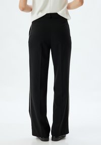 Zwarte wijde broek met een strak ontwerp, voorzien van zijsplitten en een zachte textuur, gestyled met een tailleband en achterzakken.