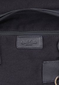 Zwarte stoffen binnenkant van een tas met een rits en een gestikt leren label met de tekst "Guest Leader studio."