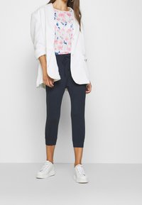 Vit oversized blazer över en blommönstrad ljus topp, parat med mörka cropped byxor och vita sneakers. Slät tyg, avslappnad passform.