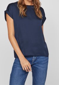 Námořnická modrá blůza s krátkými rukávy z hladké látky, s kulatým výstřihem a ohrnutými manžetami, kombinovaná s modrými džíny.