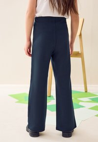 Pantalones anchos de talle alto en azul marino, confeccionados con un material suave, que presentan un acabado liso y un diseño sencillo. Se ven zapatos de plataforma negros.
