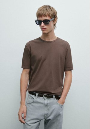 Braunes Baumwoll-T-Shirt mit kurzen Ärmeln und Rundhalsausschnitt, getragen mit hellgrauen Jeans und einem geflochtenen schwarzen Gürtel. Einfarbig; keine Muster.