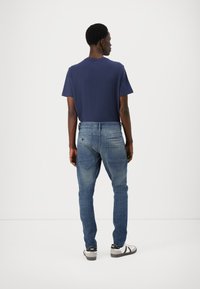 Mornarsko modra bombažna majica v kombinaciji s svetlo modrimi kavbojkami, ki imajo subtilno zbledel videz, in črno-belimi športnimi čevlji.