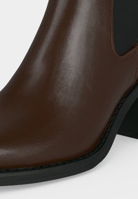 Bottine en cuir marron foncé lisse avec un panneau latéral élastique noir et un talon et une semelle noirs robustes.