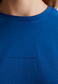 Niebieska bawełniana koszulka z prążkowaną fakturą i okrągłym dekoltem. Z przodu znajduje się subtelny, ciemny nadruk "Marc O'Polo DENIM".