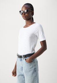 White short-sleeve T-shirt with a scoop neckline, paired with light blue high-waisted denim jeans and a black belt. Sun glasses complete the look.