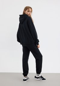 Svart oversized hoodie och matchande joggers i mjukt tyg. Har ribbade muddar, huva och logotypdetaljer på svarta sneakers.