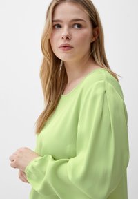 Vihreä blouse, joka on valmistettu kevyestä kankaasta, sekä pyöreä kaula-aukko että pitkät puffihihat, joissa on rypytetty hihansuu.