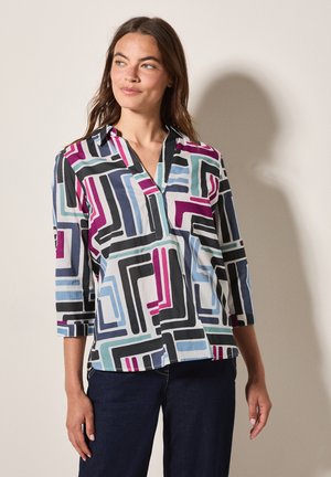 Camisa multicolor con patrones geométricos en negro, verde azulado, púrpura y azul. Tiene un escote en V y mangas tres cuartos.