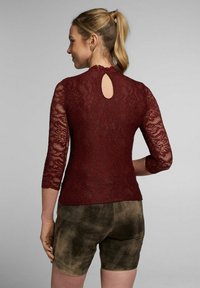 Bordeaux kanten top met driekwart mouwen, voorzien van een sleutelgatdetail aan de achterkant. Gecombineerd met bruine, gestructureerde shorts.