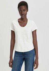 T-shirt bianco a maniche corte con scollatura rotonda e vestibilità comoda, realizzato in tessuto morbido, abbinato a jeans blu.