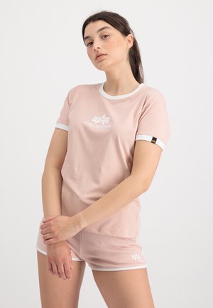 Helles rosa Sportoberteil mit weißem Besatz und Logo auf der Brust, kombiniert mit passenden Shorts, die weiße Akzente am Saum aufweisen. Weiche Stofftextur.