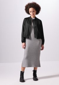 Veste bomber noire avec taille élastique, portée sur une robe midi gris côtelée avec des fentes sur les côtés, associée à des bottines à lacets noires.