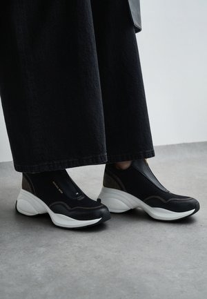 Mustad libised jalatsid, millel on võrgust ülemine osa ja tekstureeritud detailid, esitledes tugevdatud valget tallat, ning külgedel diskreetne bränding.