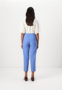 White textured cropped blouse and light blue tailored pants, paired with brown shoes, viewed from the back against a plain background.