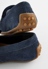 Granatowe zamszowe loafersy z gumowymi podeszwami, z fakturowanymi akcentami i zaokrąglonymi uchwytami, prezentujące płaski, smukły design.