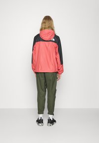 Červeno-černá bunda s kapucí a elastickými manžetami, doplněná olivově zelenými kalhotami a černými teniskami s bílým vzorem.