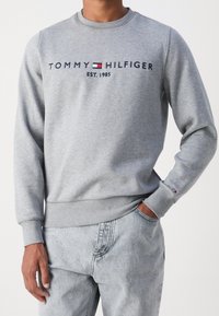 Sudadera gris de mezcla de algodón, con puños y dobladillo acanalados, con el logo "TOMMY HILFIGER" y el año "EST. 1985" en texto azul marino.