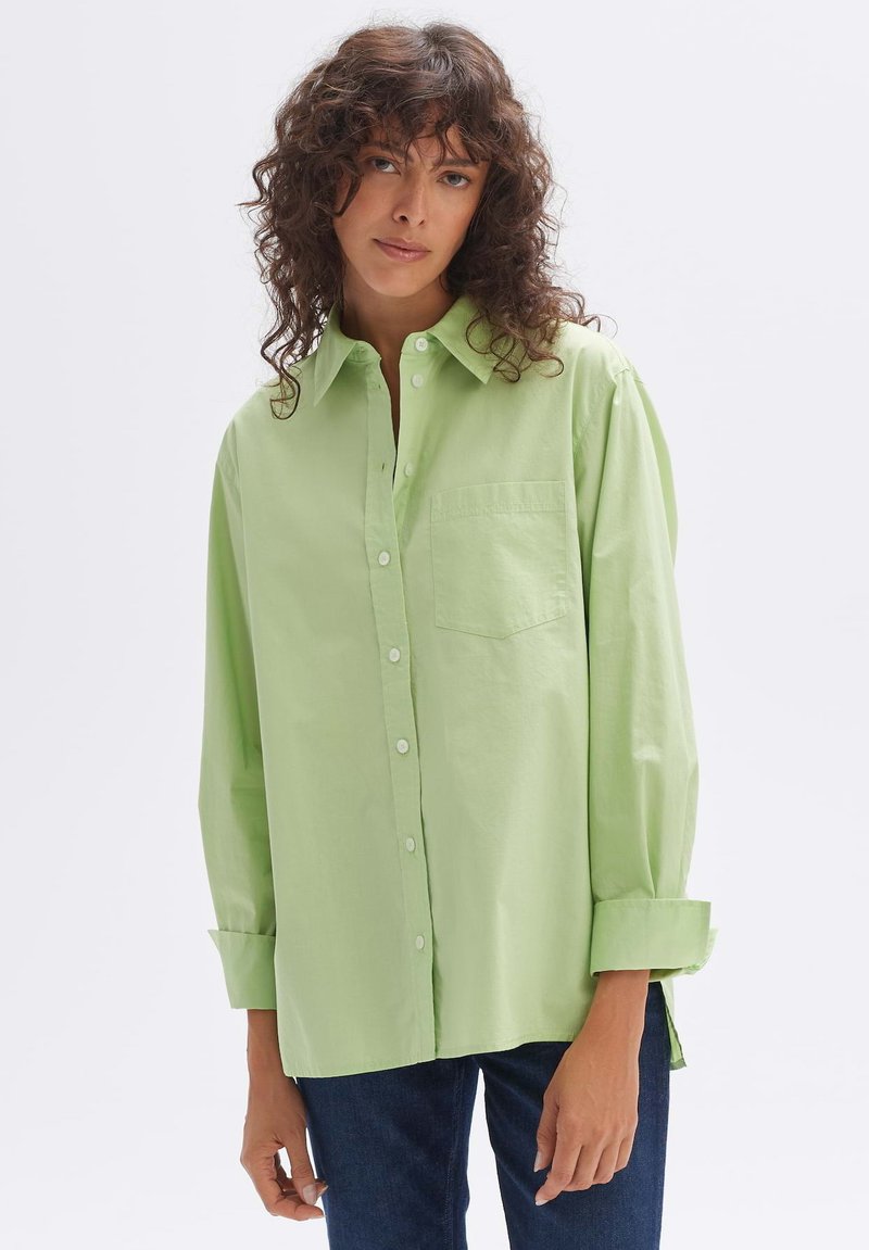 Light green button-up shirt made of cotton, featuring a chest pocket, long sleeves with rolled cuffs, and a relaxed fit.