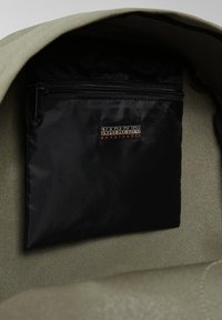 Interno di uno zaino in tessuto verde con una tasca con zip nera che presenta un'etichetta ricamata "NAPAPIJRI geographic". Materiali texturizzati e resistenti.