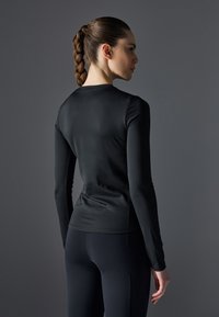 Svart langermet athletic topp laget av glatt, stretchy materiale, med en tettsittende design og rund hals, sammen med svarte leggings.