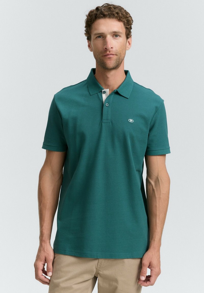 Teal polo skjorte lavet af bomuld, med krave-nakke, to-knap lukning, korte ærmer og et lille logo på brystet.