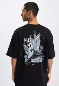 Tricou negru din bumbac cu un grafic mare de culoare gri reprezentând o porumbiță, cu textul "ZILELE DE ALTĂDATĂ", mâneci scurte și o croială lejeră.