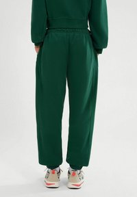 Pantalones de chándal verdes de corte holgado con una cintura elástica y puños en los tobillos. Material suave, con bolsillos laterales y una textura lisa.