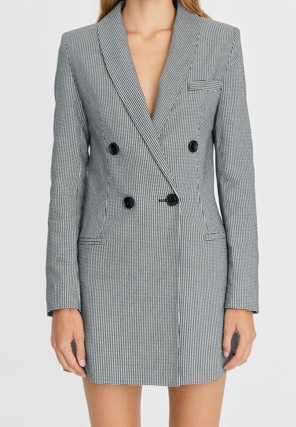 Robe blazer croisée en pied-de-poule noir et blanc. Elle présente un col à revers cranté, des boutons noirs et des poches avant.