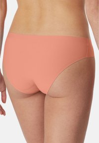 Pfirsichfarbener, nahtloser Bikini-Strings mit einer glatten Textur und moderater Bedeckung, der ein schlichtes Design und keine sichtbaren Beschläge aufweist.