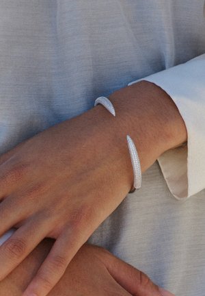Sidabrinė apyrankė su tekstūruota paviršiumi, turinti smailius galus. Dizainas yra elegantiškas ir minimalistinis, akcentuojantis metalinį blizgesį.