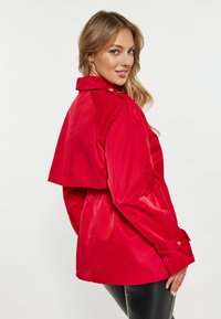Rode, glanzende jas met een cropped ontwerp, een ceintuur in de taille en knoopmanchetten. Beschikt over een kraag en elegante stiksels.