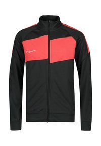 Zwarte sportjack met rode bovenpanelen, ritsvoorkant, hoge kraag en Nike-logo op de borst. Gemaakt van glad, lichtgewicht materiaal.