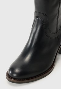 Bottines en cuir noir avec un bout arrondi, des détails de couture subtils et un petit talon empilé. Fini texturé et accent de semelle marron.