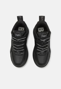 Svarta sportskor med en slät syntetlär övre, grå snören, vadderad krage och dragflikar för enkel påtagning. Varumärkeslogotyp på tungan.