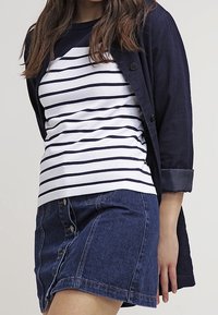 Marinblå cardigan över en vit och marinblå randig t-shirt, i kombination med en blå denimkjol med knappar. Mjuk tygkvalitet, avslappnad passform och kontrasterande färger.