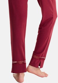 Pantalons de pyjama bordeaux en tissu doux, avec des accents en dentelle transparente aux poignets et des fentes latérales, présentés avec un pied à découvert.